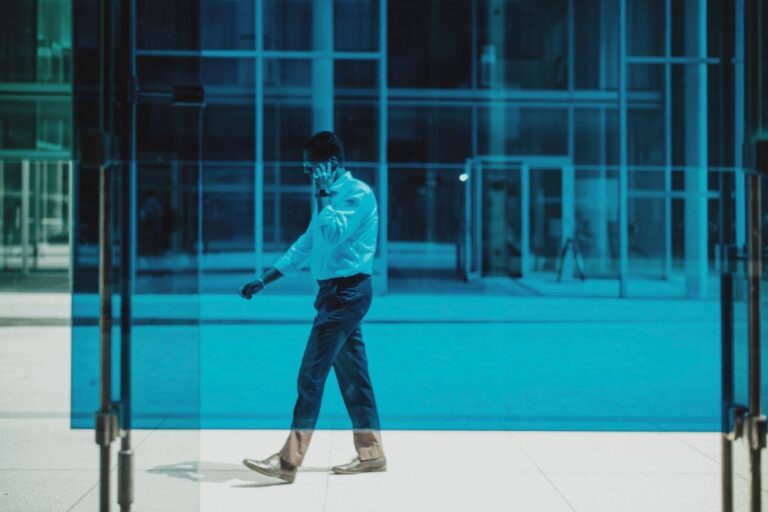 Professional man walks while on a phone call outside a modern glass building