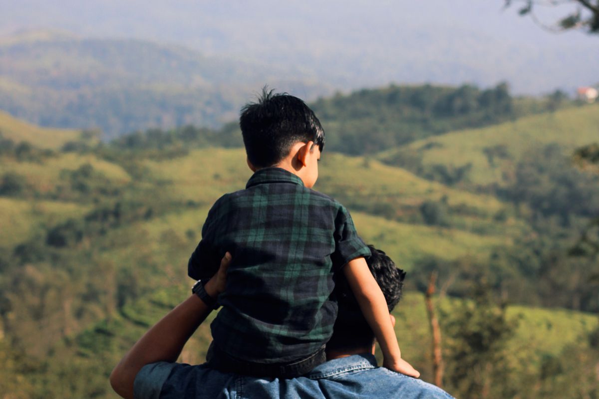 son on fathers shoulders in countryside